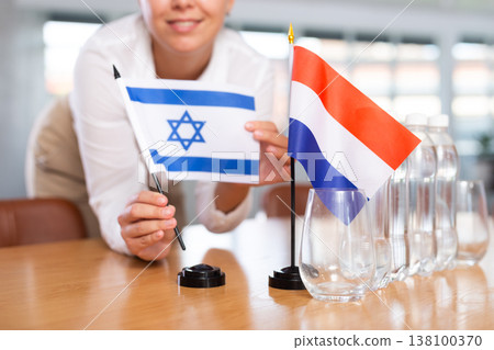 Employee of delegation prepares negotiating table - sets up flag of Netherlands and Israel Employee of delegation prepares negotiating table - sets up flag of Netherlands and Israel 138100370