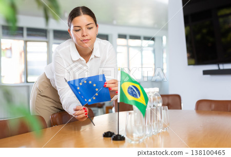 Positive young woman putting little flag of European Union on table next to the flag of Brazil Positive young woman putting little flag of European Union on table next to the flag of Brazil 138100465