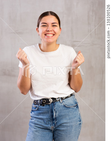 Cheery young woman posing happily against gray background Cheery young woman posing happily against gray background 138100526