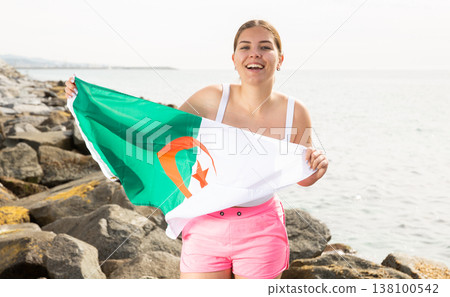 Portrait of positive girl with the flag of Algeria on the seashore on sunny day Portrait of positive girl with the flag of Algeria on the seashore on sunny day 138100542