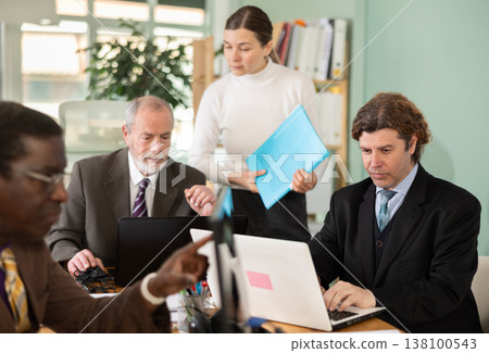 Woman with documents is standing next to senior male colleague with laptop Woman with documents is standing next to senior male colleague with laptop 138100543