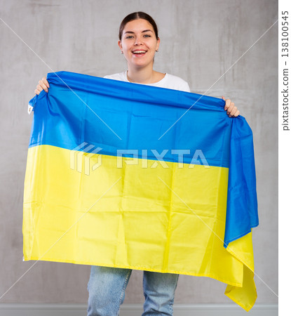 Joyous young woman holding Ukraine flag against unicoloured background Joyous young woman holding Ukraine flag against unicoloured background 138100545