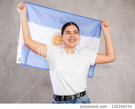 Excited young woman holding state flag of Argentina against gray wall background indoors 138100554