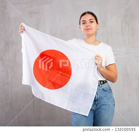 Calm girl stands with flag of Japan. Isolated on gray background Calm girl stands with flag of Japan. Isolated on gray background 138100595