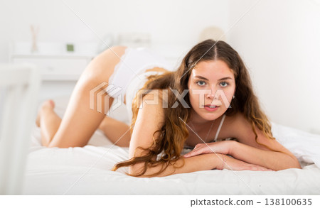 Long-haired young brunette in lingerie lying on bed Long-haired young brunette in lingerie lying on bed 138100635