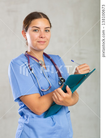 Young happy female nurse writing in file with papers Young happy female nurse writing in file with papers 138100673