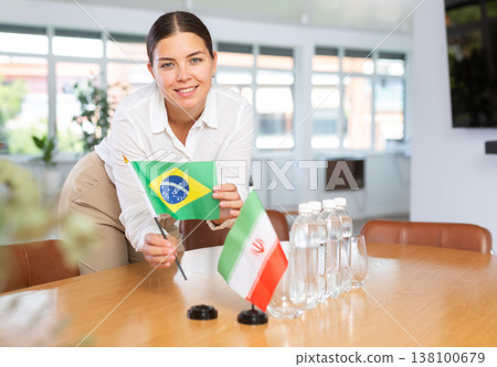 Positive young woman putting little flag of Brazil on table next to the flag of Iran 138100679