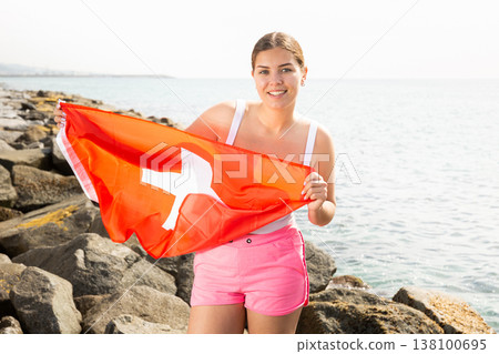 Slender girl with the flag of Switzerland on the lakeshore on sunny summer day 138100695