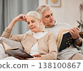 Old couple, relax on sofa and reading book, retirement and support with time together at home. People in living room, knowledge and literature, leisure and hobby with love and comfort with story 138100867