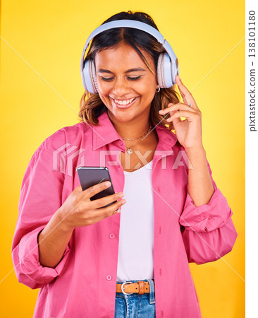 Headphones, cellphone and young woman in a studio listening to music, playlist or radio and networking. Happy, phone and female model from Mexico streaming a song or album by yellow background. 138101180