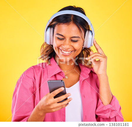 Headphones, phone and young woman in a studio listening to music, playlist or radio and networking. Happy, cellphone and female model from Mexico streaming a song or album by yellow background. 138101181