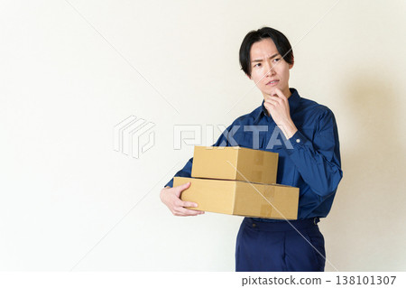 A delivery person holding a cardboard box and deep in thought. 138101307