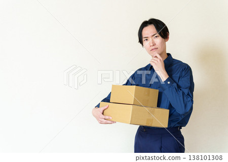 A delivery person holding a cardboard box and deep in thought. A delivery person holding a cardboard box and deep in thought. 138101308