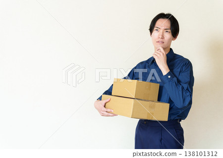 A delivery person holding a cardboard box and deep in thought. A delivery person holding a cardboard box and deep in thought. 138101312
