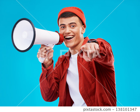 Portrait, bullhorn and young man in studio pointing for an announcement or speech at a rally. Happy, smile and male activist on stool with megaphone for loud communication isolated by blue background 138101347