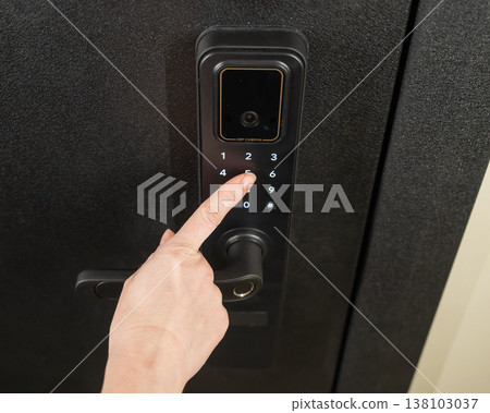 A woman opens a modern smart door lock with a digital keypad using a code. 138103037