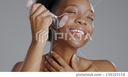Black woman, face with roller and massage for skincare and beauty, natural cosmetics and treatment on white background. Wellness, dermatology and skin glow, rose quartz crystal and tools in studio 138103158