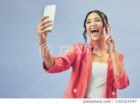 Smile, selfie and happy woman with a peace sign from social media and profile picture for creative job in studio. Influencer and makeup with career fashion with blue background and emoji hand gesture 138103347