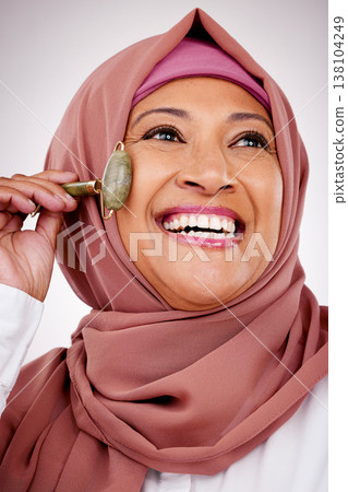 Muslim woman, facial roller and skin care in studio with quartz for dermatology, cosmetics and glow. Happy mature female person with islam hijab, face massage and beauty on a white background Muslim woman, facial roller and skin care in studio with quartz for dermatology, cosmetics and glow. Happy mature female person with islam hijab, face massage and beauty on a white background 138104249