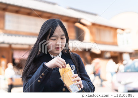 Female students in school uniforms enjoy the local specialty, sweet potato chips, against the backdrop of retro buildings in Koedo Kawagoe. 138105093