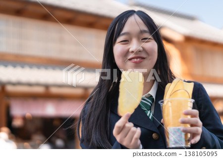 Female students in school uniforms enjoy the local specialty, sweet potato chips, against the backdrop of retro buildings in Koedo Kawagoe. Female students in school uniforms enjoy the local specialty, sweet potato chips, against the backdrop of retro buildings in Koedo Kawagoe. 138105095