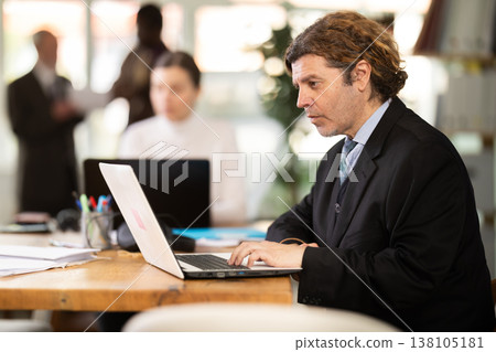 Man sitting at desk is working on laptop computer. Working day in office Man sitting at desk is working on laptop computer. Working day in office 138105181