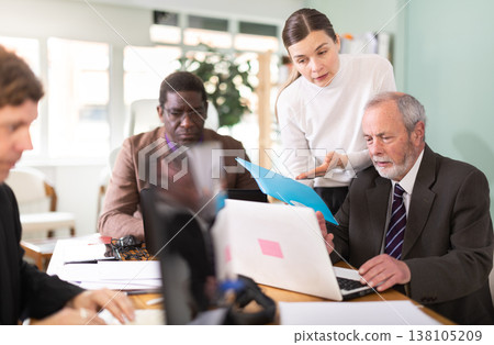 Woman with documents is standing next to senior male colleague with laptop Woman with documents is standing next to senior male colleague with laptop 138105209