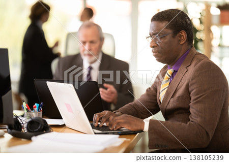 African man sitting at desk is working on laptop computer. Working day in office 138105239