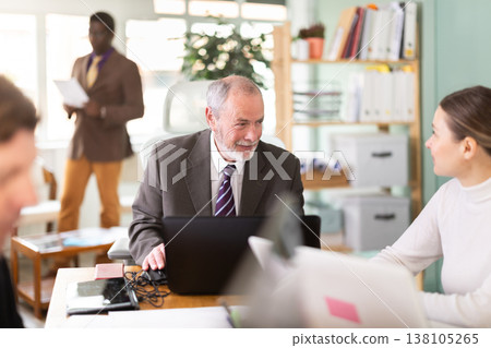 Senior man sitting at desk is working on laptop computer. Working day in office Senior man sitting at desk is working on laptop computer. Working day in office 138105265