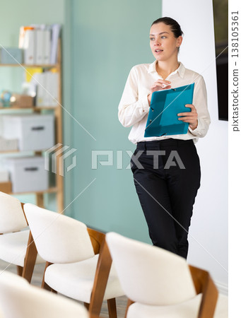 Female coach with folder with papers standing near blackboard in classroom Female coach with folder with papers standing near blackboard in classroom 138105361