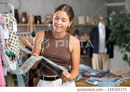 Girl customer choose scarf in store, and buyer carefully examines product. Girl customer choose scarf in store, and buyer carefully examines product. 138105375