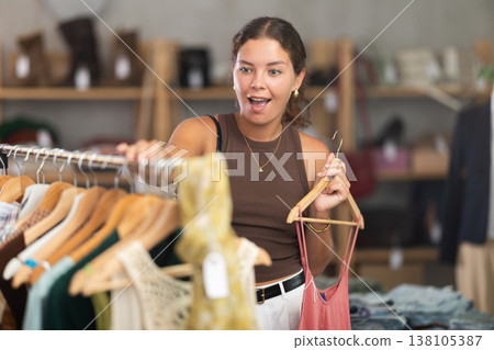 Girl customer choose crop top in store, and buyer carefully examines product. Girl customer choose crop top in store, and buyer carefully examines product. 138105387