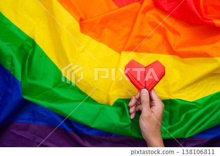 Hand holding red origami heart on rainbow flag Hand holding red origami heart on rainbow flag 138106811