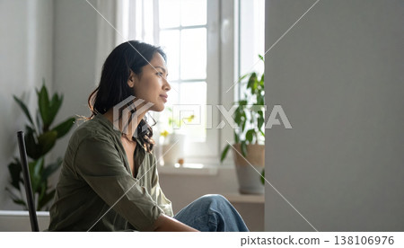 Mental wellness, depression. Thoughtful woman sits by window, gazing outside with serene expression 138106976