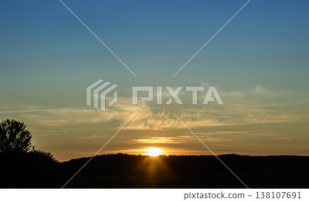 Vibrant sunset seen over rolling hills with soft clouds creating a serene atmosphere in the early evening sky Vibrant sunset seen over rolling hills with soft clouds creating a serene atmosphere in the early evening sky 138107691