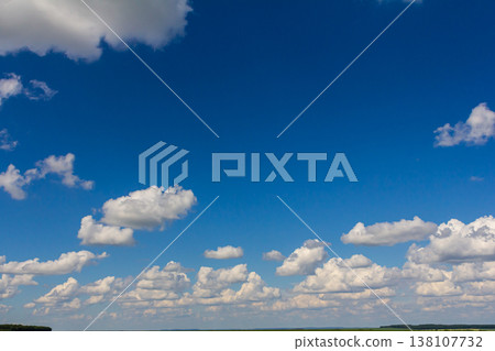 Bright blue sky with fluffy clouds gently floating above a serene landscape during daylight hours Bright blue sky with fluffy clouds gently floating above a serene landscape during daylight hours 138107732