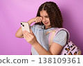 Emotional Young Girl with Curly Hair Crying While Holding a Smartphone Against Purple Background 138109361