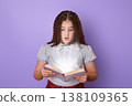 Curious Girl Reading a Book with Fascination Against a Soft Purple Background 138109365