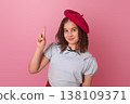 A Young Girl in a Beret Playfully Posing Against a Pink Background with a Finger Raised 138109371