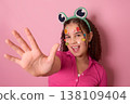 Joyful Girl Playfully Displaying Candy-Decorated Face Against a Vibrant Pink Background 138109404
