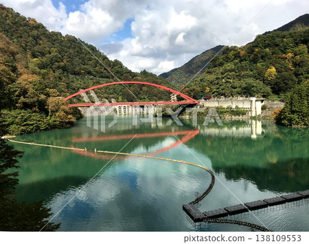 The Shin-Yamahiko Bridge spanning Lake Unazuki in the Kurobe Gorge and its reflection on the water's surface. 138109553