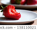Close-up of a juicy half-eaten strawberry on a white plate 138110021
