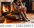 Cozy evening by fireplace: female relaxing with hot drink in warm sweater and socks 138110053