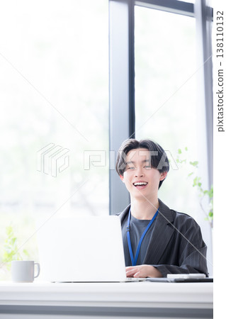 A young businessman at his computer, looking directly at the camera: A refreshing business scene showcasing the growth and success of a young employee. 138110132