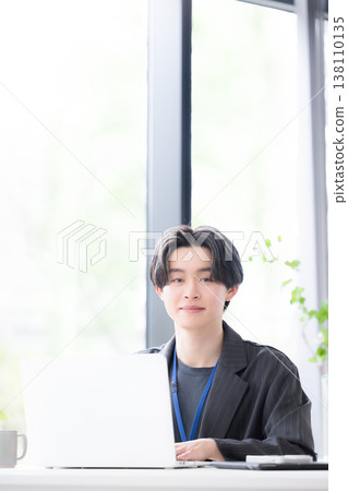 A young businessman at his computer, looking directly at the camera: A refreshing business scene showcasing the growth and success of a young employee. A young businessman at his computer, looking directly at the camera: A refreshing business scene showcasing the growth and success of a young employee. 138110135