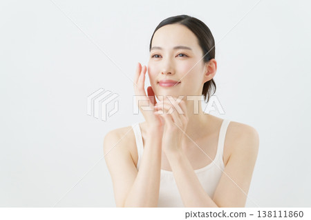 A skincare image of a young woman with her hand on her cheek against a white background. A skincare image of a young woman with her hand on her cheek against a white background. 138111860