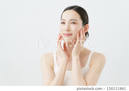 A skincare image of a young woman with her hand on her cheek against a white background. A skincare image of a young woman with her hand on her cheek against a white background. 138111861