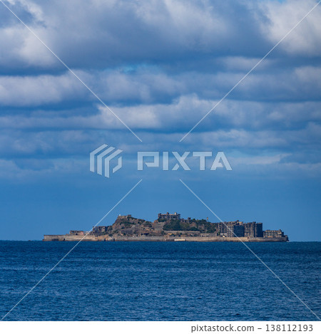A panoramic view of Gunkanjima Island floating in the distant sea under a blue sky. A panoramic view of Gunkanjima Island floating in the distant sea under a blue sky. 138112193