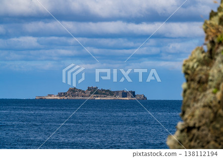 A panoramic view of Gunkanjima Island floating in the distant sea under a blue sky. A panoramic view of Gunkanjima Island floating in the distant sea under a blue sky. 138112194