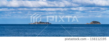 A panoramic view of Gunkanjima Island floating in the distant sea under a blue sky. A panoramic view of Gunkanjima Island floating in the distant sea under a blue sky. 138112195